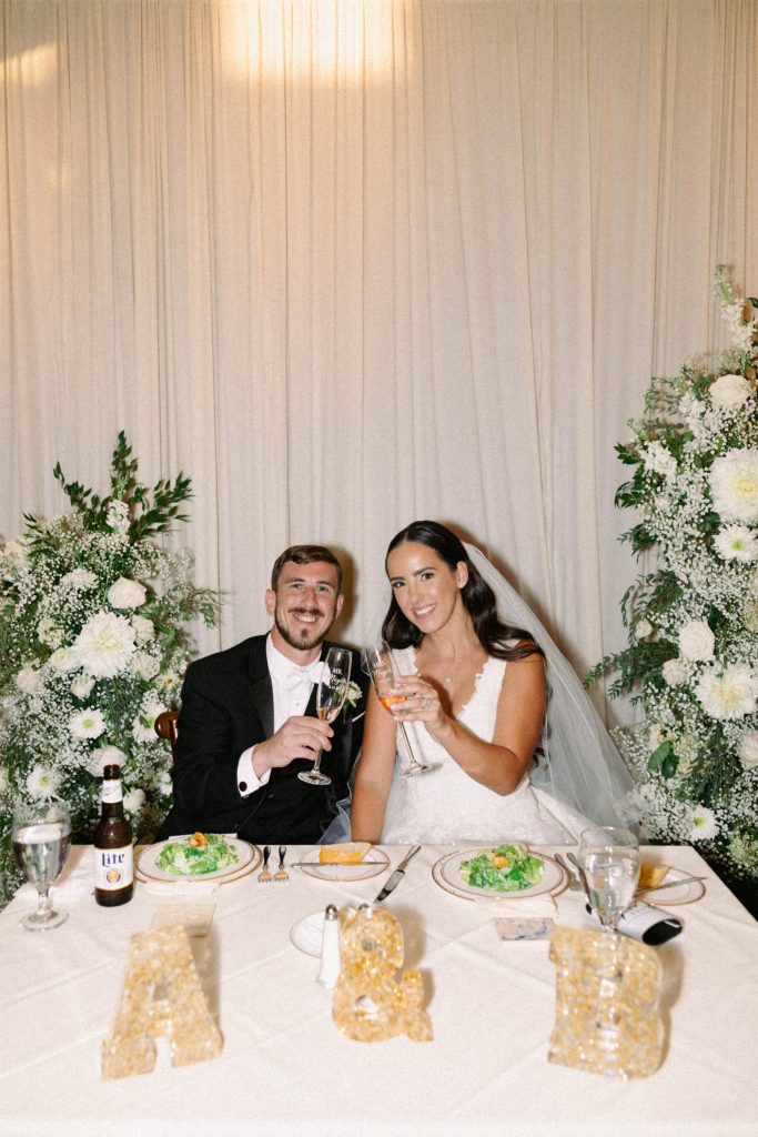 Bride and groom smiling and raising a glass together at their wedding reception.